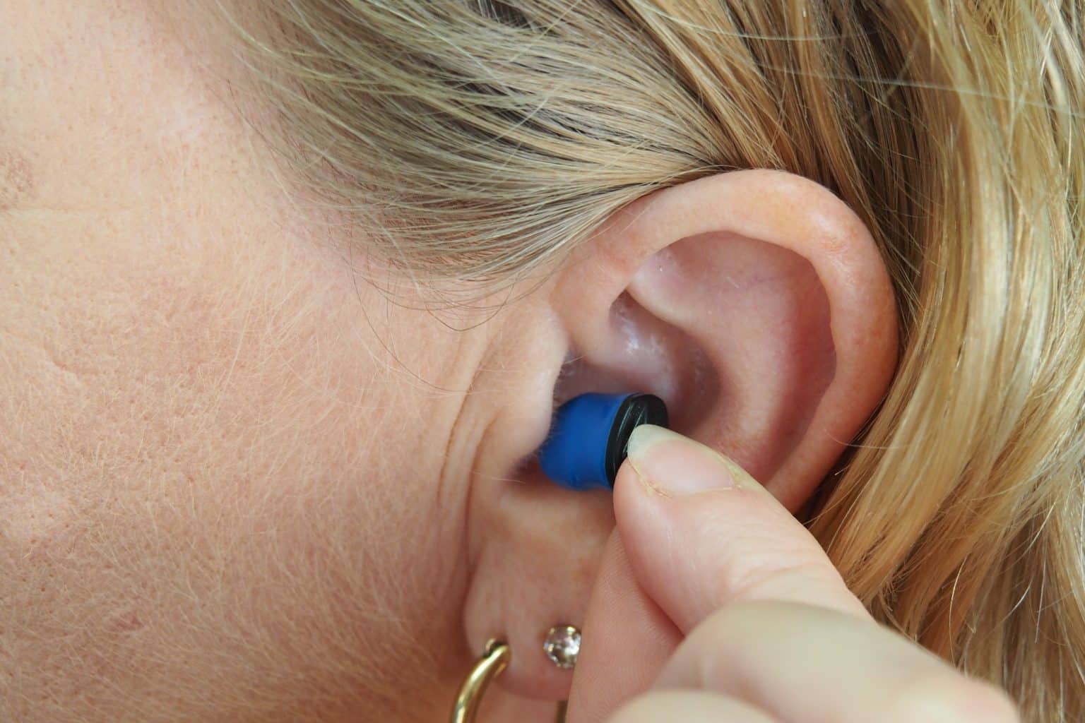A blonde woman from Wichita Falls inserts blue hearing aid into her ear after performing hearing aid maintenance