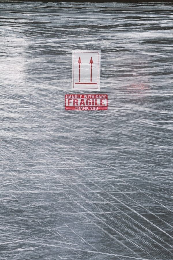 White sign with two red arrows pointing up. Underneath the arrows is a fragile warning label.